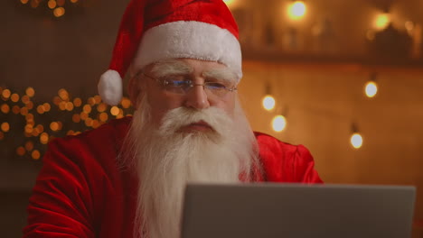 santa claus using laptop in living room. portrait of thoughtful santa claus typing with modern laptop in decorated house. high quality 4k footage