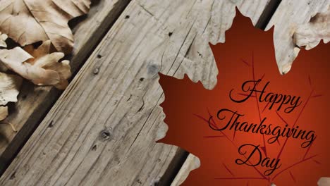 animation of happy thanksgiving day text over autumn leaf on wooden boards background