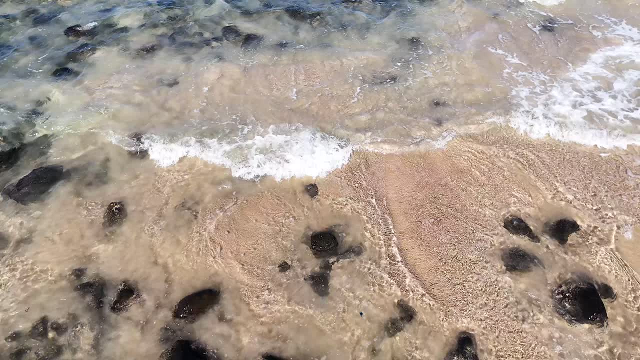 파도가 부드럽게 모래 해변의 바위 위에 어