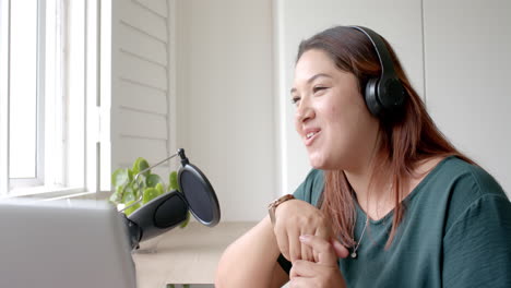 happy plus size biracial woman in headphones podcasting with laptop at home, copy space, slow motion