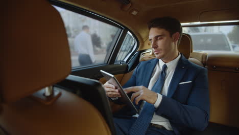 focused male professional reading documents on digital tablet in modern car.