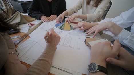 a team of architects and designers gather around a table, examining building plans and discussing various material samples for a construction project