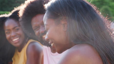 three friends sitting outside in the sun laughing, close up