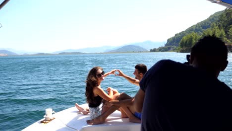 young pair sitting on bow of boat and posing to unrecognizable photographer. happy couple in love spending time together on deck of ship and enjoying summer travel. concept of vacation or holiday.