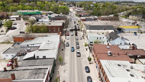 aerial backwards shot showing cars driving on road in canadian small village named grimsby and ontario lake in background