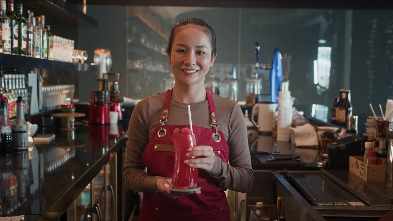 Portræt af ung servitrice, der holder en frisk cocktail på en café