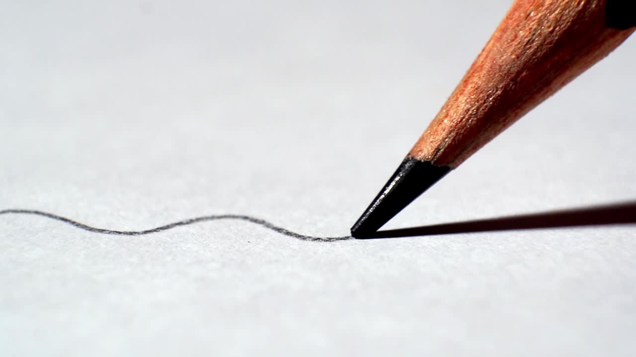 Macro close‑up of pencil tip drawing a single squiggle line across paper