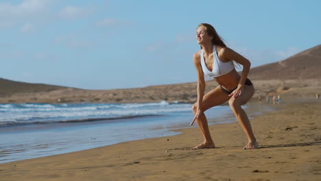 Una-Chica-Con-Pantalones-Cortos-Y-Camiseta-Deportiva-Realiza-Saltos-Con-Sentadillas-En-La-Playa-Cerca-Del-Océano-En-Las-Islas-Canarias.-Estilo-De-Vida-Saludable-Y-Fitness-Durante-Las-Vacaciones.-Cuerpo-Hermoso-Y-Saludable