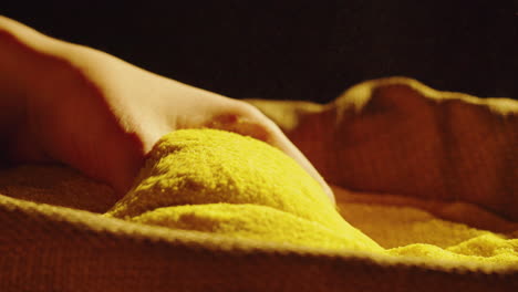 a close-up of a hand interacting with and pouring vibrant yellow cornmeal into a sack