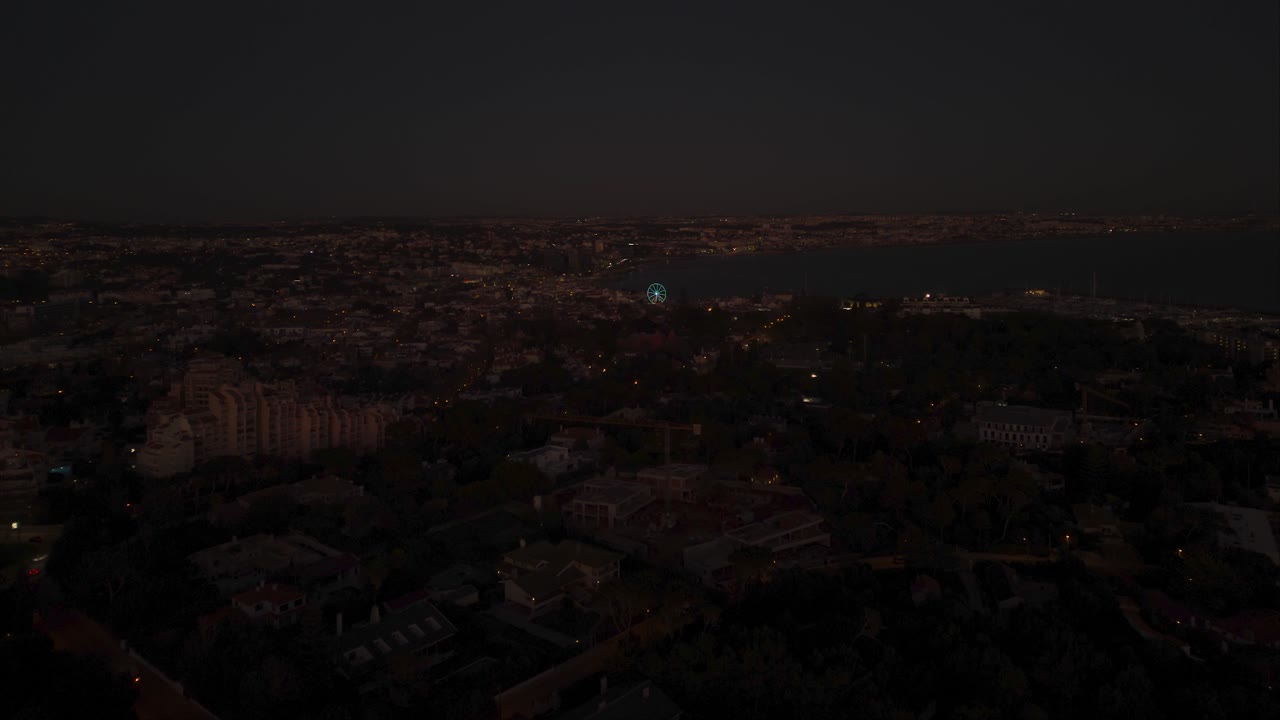 Ripresa aerea panoramica con drone che domina il centro città, la ruota panoramica, la spiaggia e la Marina di Cascais, di notte, a Lisbona, Portogallo