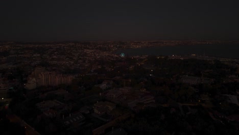 Aerial,-pan,-drone-shot-overlooking-the-downtown,-the-Ferries-wheel,-the-beach-and-the-Cascais-Marina,-at-night-time,-in-Lisbon,-Portugal