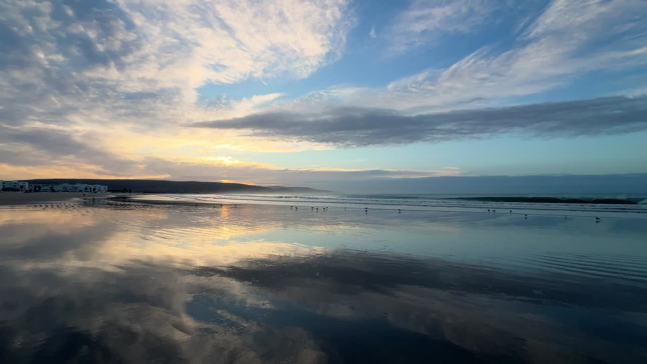 A wide, expansive shot of a pristine beach on a beautiful sunny morning, showcasing clear skies, gentle waves