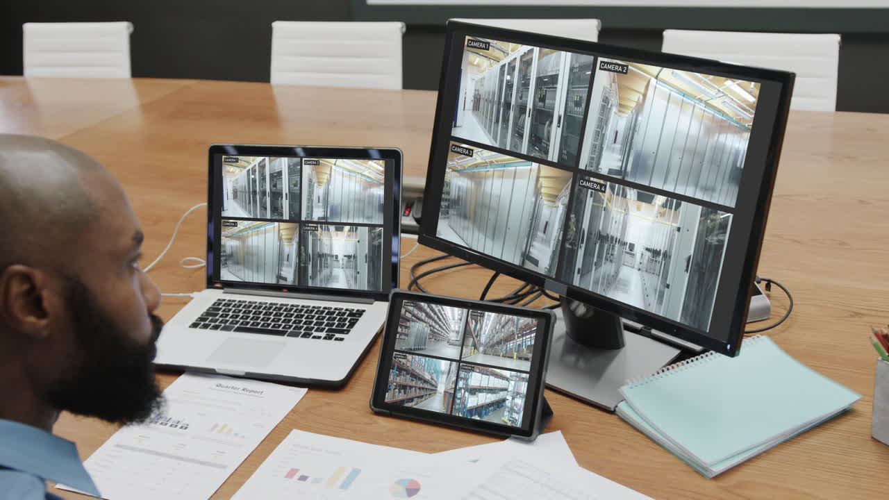 아프리카계 미국인 남성 보안 담당자가 cctv 카메라를 보고 컴퓨터 화면에서 느린 움직임을 보입니다.