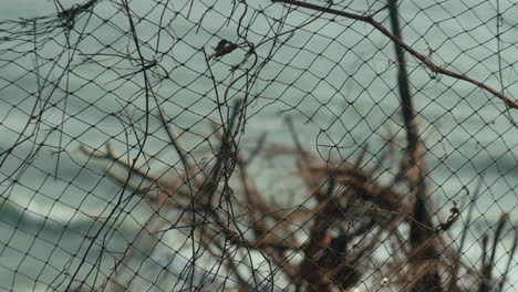 the fishing net is torn in the middle, with the sea behind it