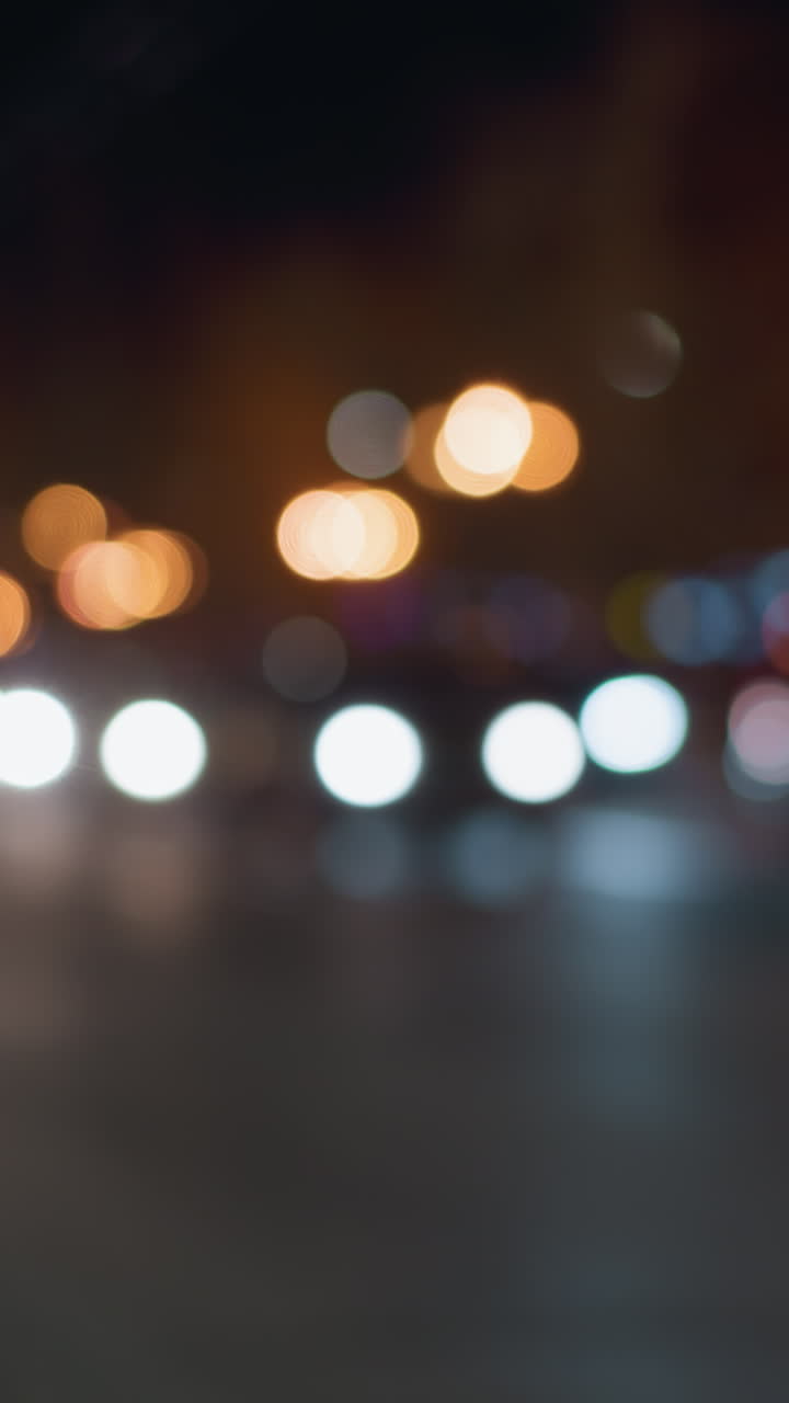vista bokeh de una escena nocturna de la ciudad con luces de automóviles borrosas y farolas en el fondo, capturada con un enfoque en un poste de la calle cercana