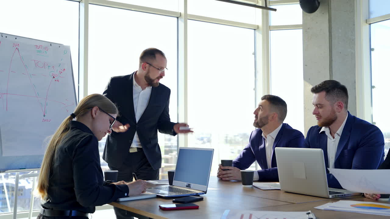 Group of young entrepreneurs indoors. Successful man talking to his partners giving his ideas. Business people sitting at the table and listen to their boss in office.