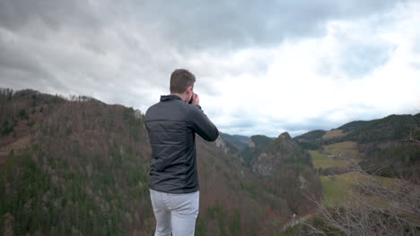 man walking on a rock with a beautiful view, taking a picture of the landscape, slow-motion