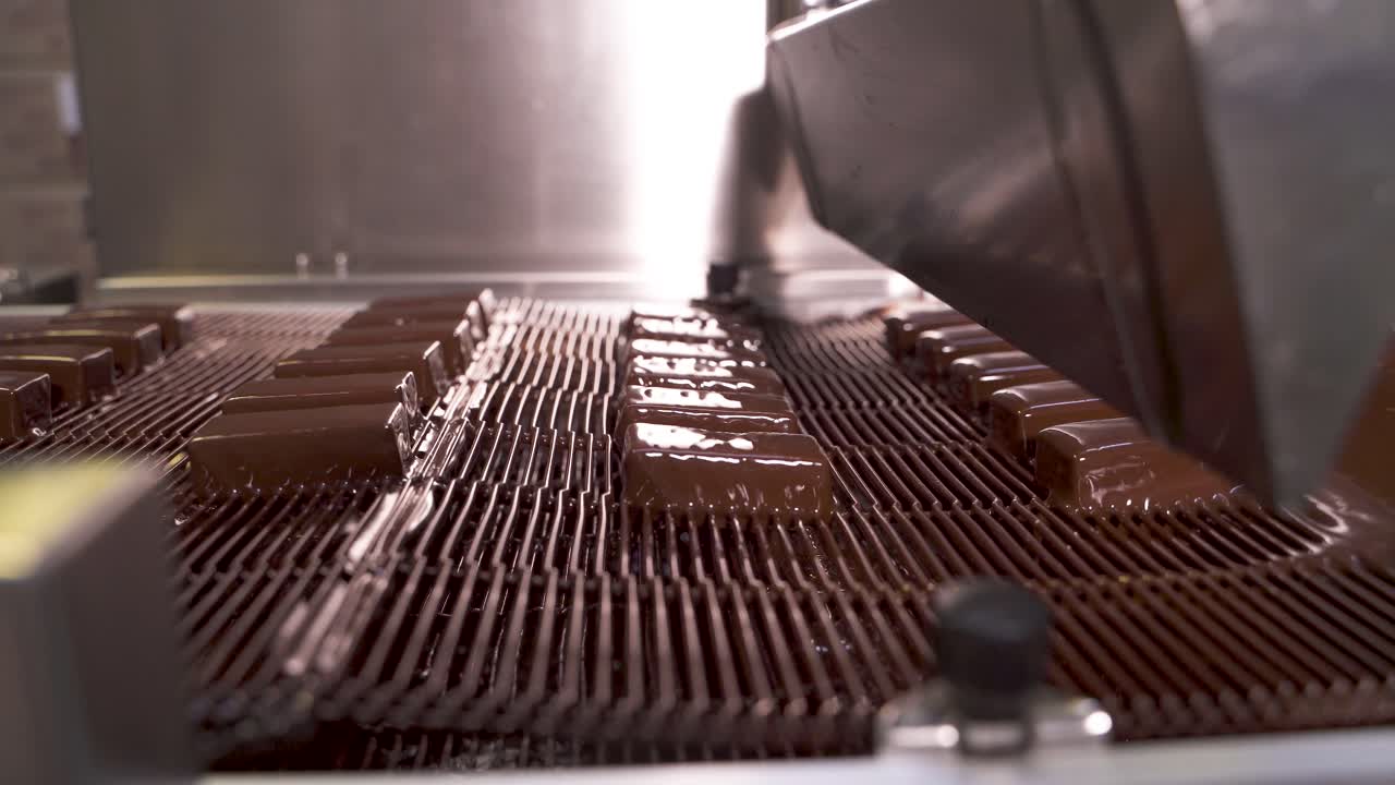 Production of chocolates in the factory. Rows of chocolates on a metal conveyor belt for coating with milk chocolate