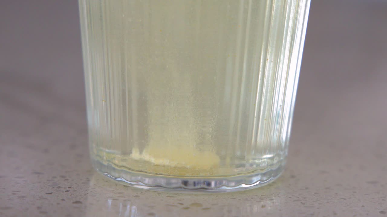 Primo piano di una compressa effervescente gialla che si dissolve e produce bolle in un bicchiere trasparente