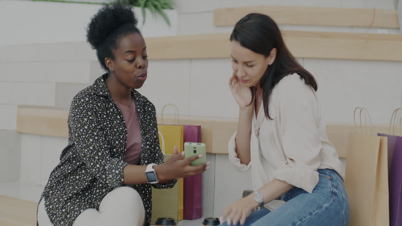 Two women looking at a smartphone in a shopping center