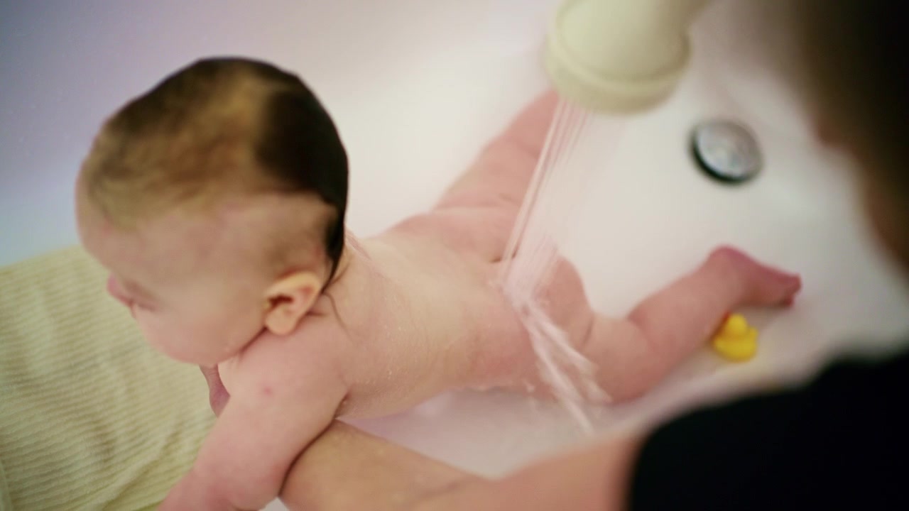 Primo piano di un neonato a cui viene fatto il bagnetto delicatamente da un assistente durante l'ora del bagno