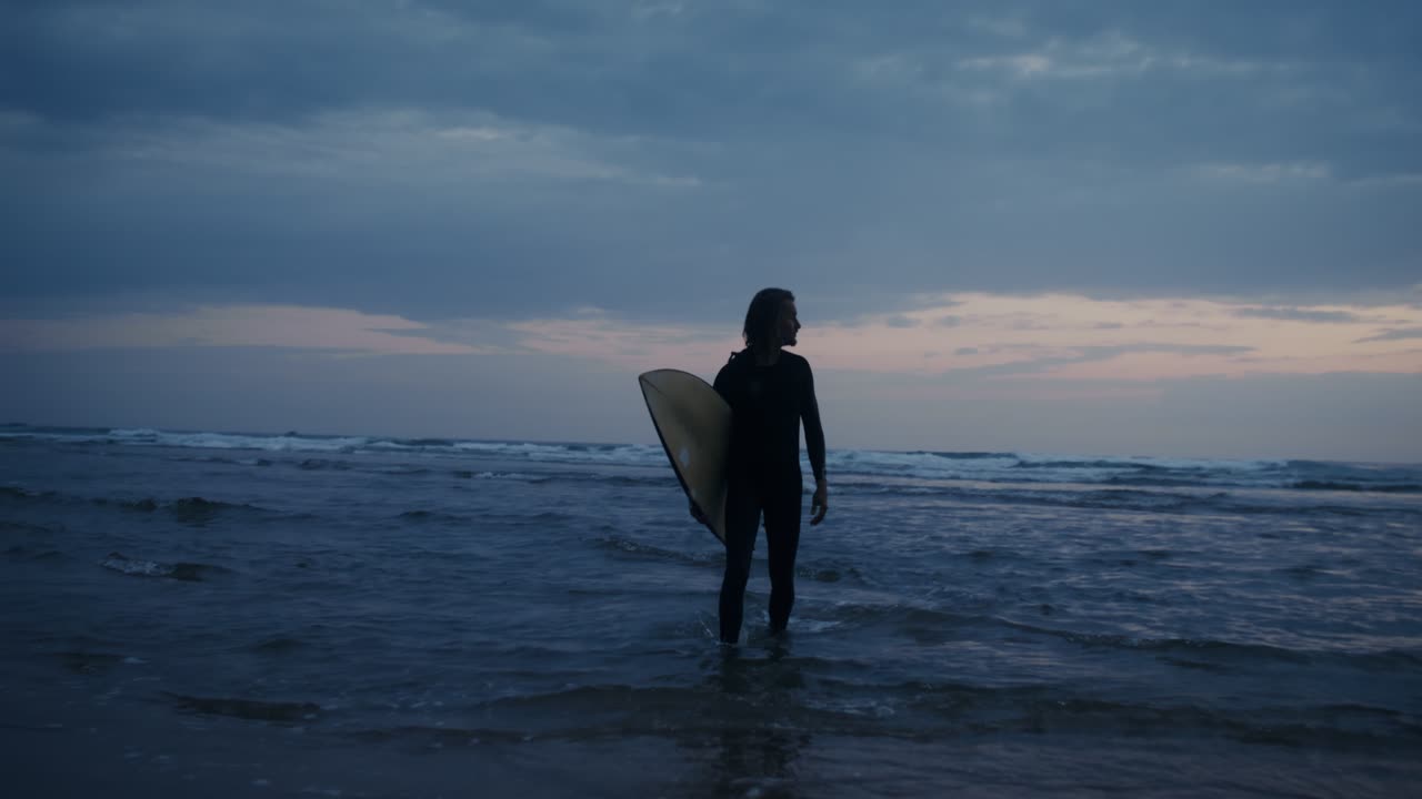 Surfista che cammina sulla spiaggia al tramonto