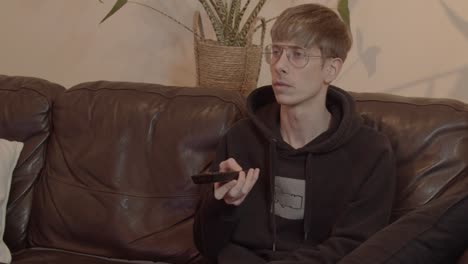 young man watches tv and uses remote control to switch channels