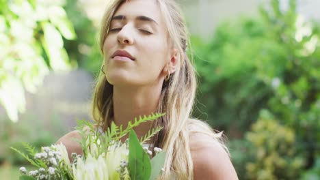 happy caucasian woman holding bunch of flowers in garden on sunny day