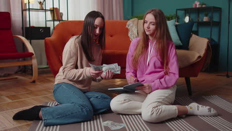 satisfied girls friends siblings calculate family budget in dollars cash write in a notebook at home