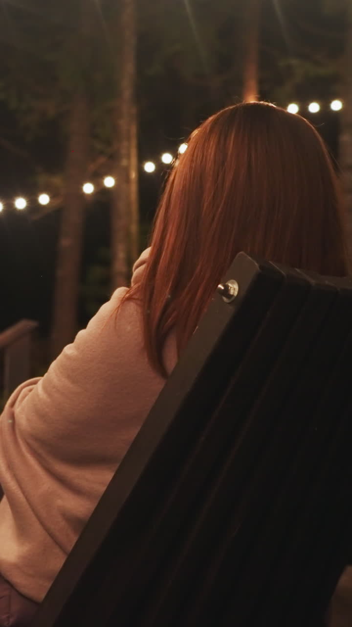 Lonely woman gazes at campfire flame sitting in armchair. Young woman seizes moment alone at camping site on chair surrounded by tranquility of nature