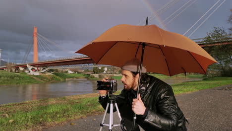 caucasian photographer takes pictures under his umbrella during a rainy day, while smiling