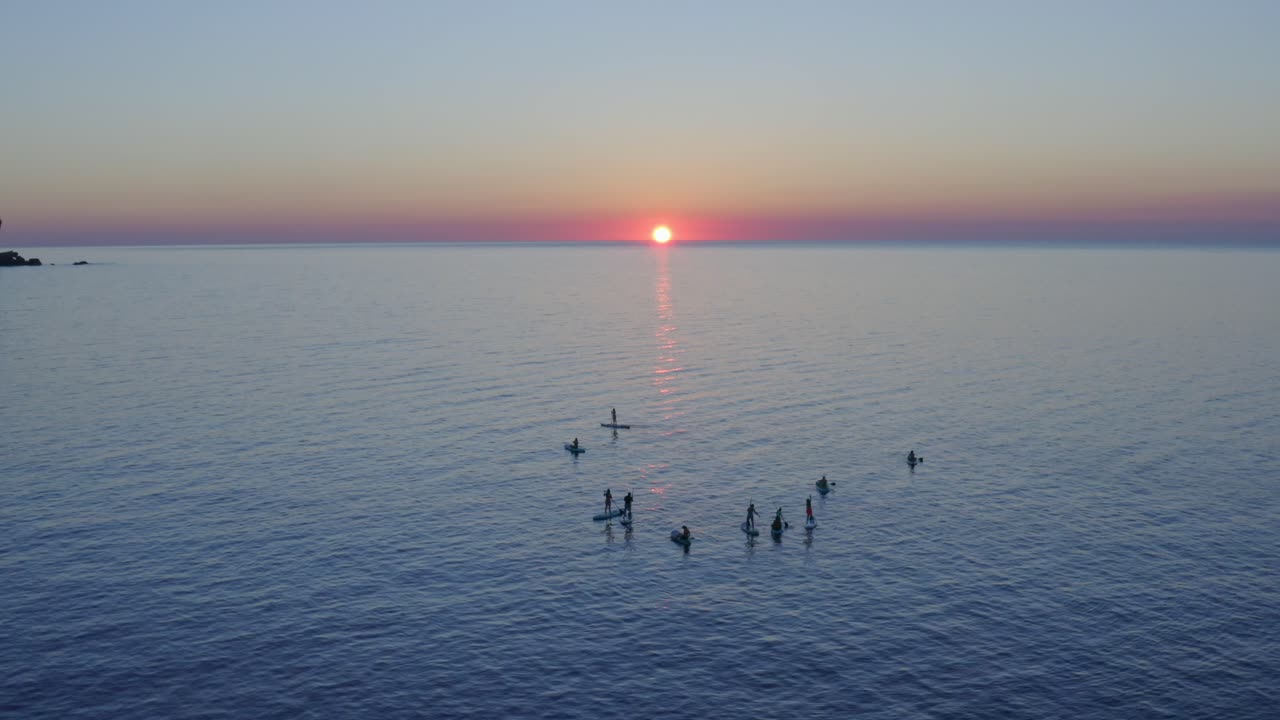 해가 지는 시점 에 메노르카 의 물 에서 떠다니는 패들 보더 들 의 실루 ⁇