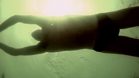 athlete swimming with the sun reflecting on the waters surface and underwater pov.