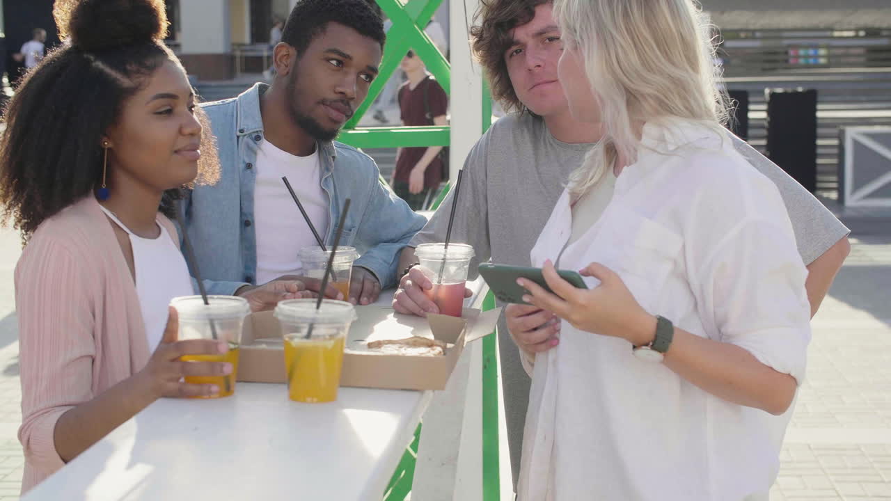 grupo de alegres jóvenes amigos tomándose selfies y divirtiéndose juntos, mientras estaban de pie en la mesa y comiendo pizza en la calle