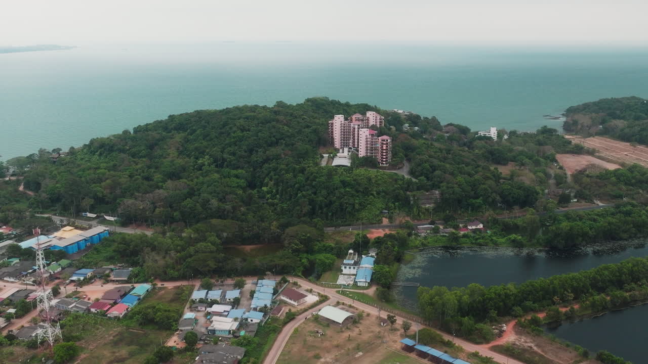 Drone che vola verso edifici in cima a una collina con vista mare a Phuket, Thailandia.