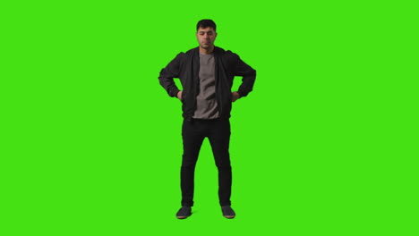 toma completa de un joven vestido casualmente de pie contra la pantalla verde cruzando los brazos y poniendo las manos en los bolsillos 1