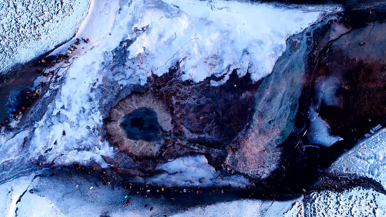 아이슬란드의 게이시르 (geysir) 에 있는 게이저 위를 드론으로 바라보는 모습. 이 게이저 밖으로 어나오고 사람들이 해가 지는 곳에서 게이저를 둘러싸고 고 있다.