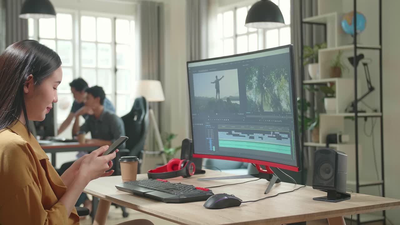 Asian Female Video Editor Works And Talking On Mobile Phone With Her Personal Computer In Office