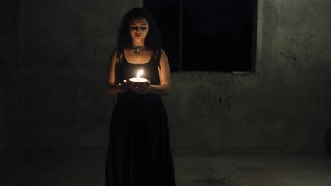 front view of woman in black dress with long hair, moving in a dark room, drops a lighted candle from her hands