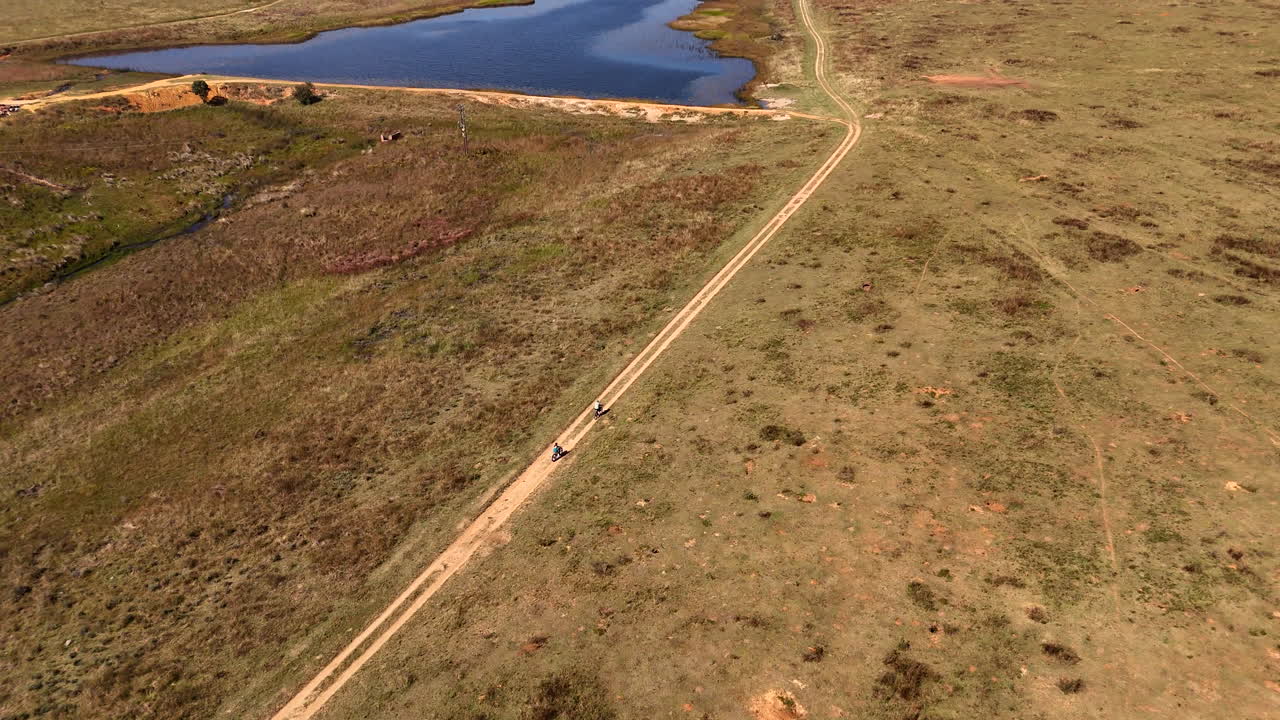 Pair of tourist cyclists on dirt road on remote game reserve, aerial tilt-up