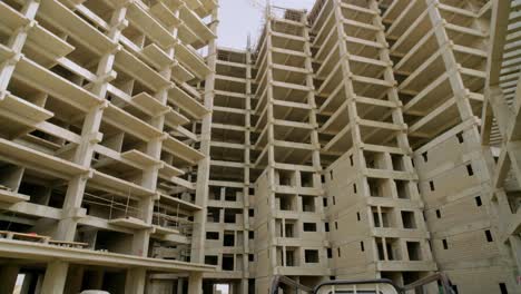 camera tilt up and pan across multiple unfinished apartment towers in karachi, revealing exposed concrete floors, open windows, scaffolding elements, and the scale of urban development in progress.
