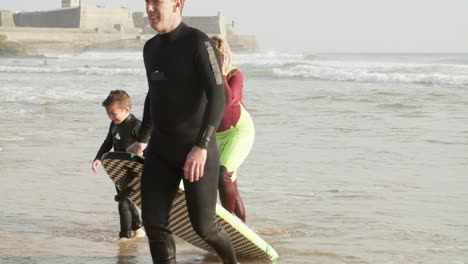 parents and son with surfboard on beach