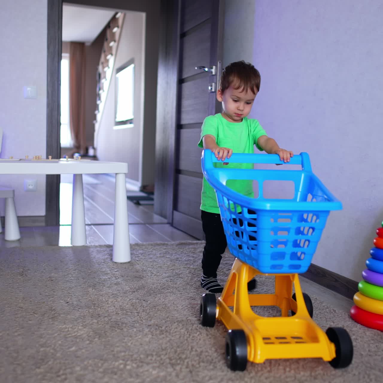 Little kid enters his room pushing a toy shopping cart. Lovely baby boy playing at home