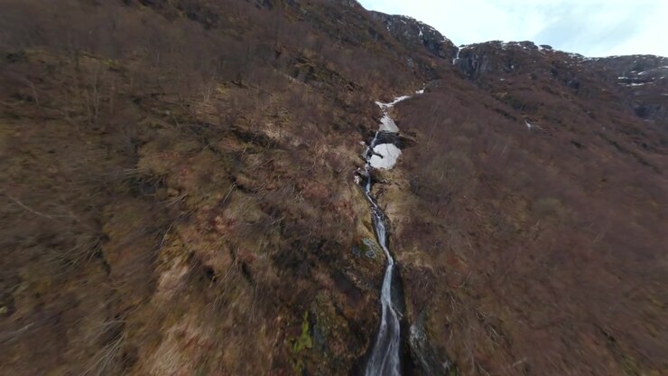 Drone che avanza lungo una valle innevata verso una cascata su una cresta montuosa in Norvegia