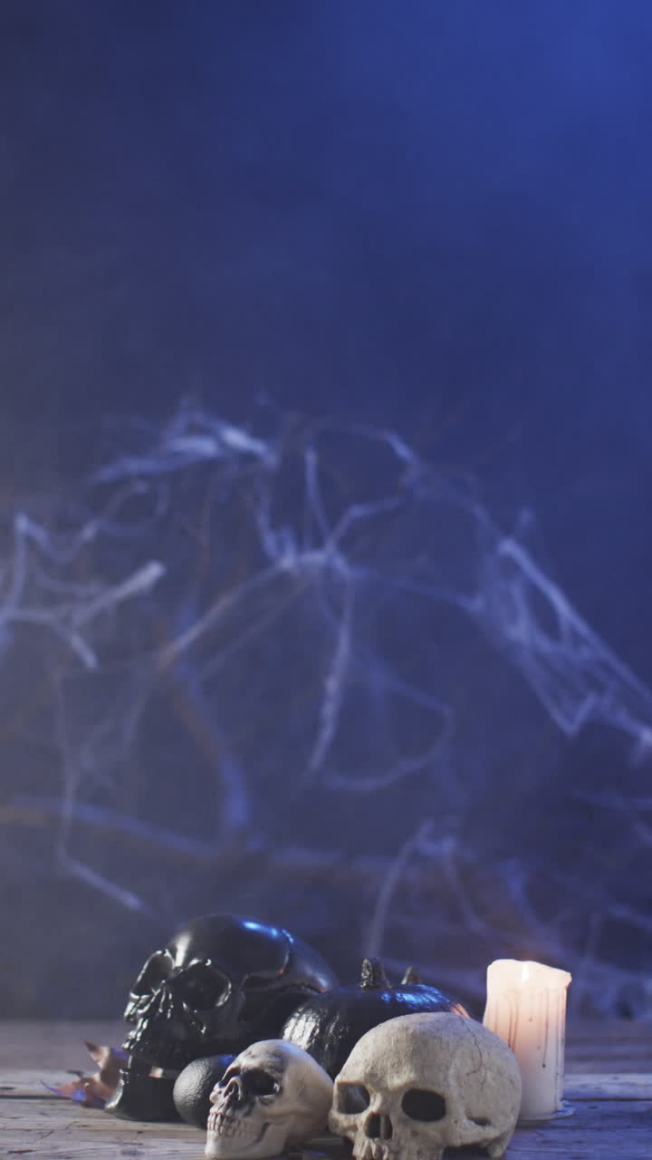 Vertical video of halloween skulls, candle and smoke with copy space on blue background