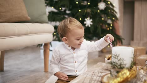 Glücklicher-Süßer-Junge-Im-Weißen-Hemd,-Der-Auf-Dem-Boden-Sitzt,-Mit-Einem-Weihnachtsbaum-Im-Hintergrund