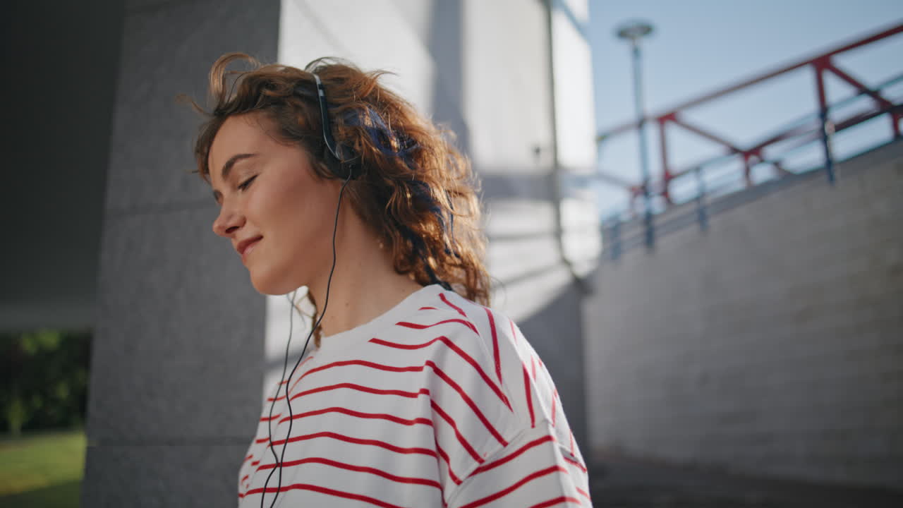 mujer disfrutar de la canción favorita en los auriculares en el distrito urbano soleado solo de cerca.