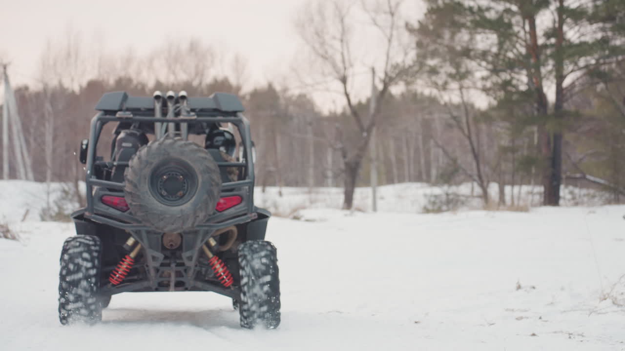 Mavi ATV UTV karlı orman açıklığında, ön ızgara ve süspansiyon detayı yakından, farlar parlıyor, sağlam lastikler ve vinç görünür, sürücü ekstrem arazi sürüşü için kontrolleri hazırlıyor.