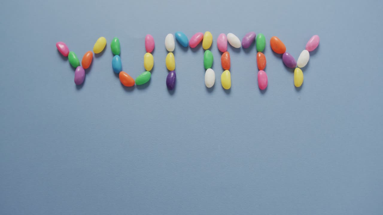 video de una vista aérea de un texto delicioso formado por dulces multicolores con espacio de copia sobre un fondo azul