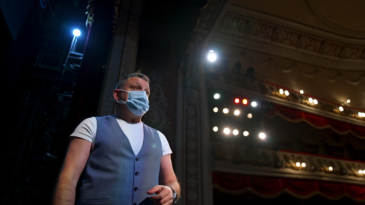 Actor in elegant suit and medical mask. Actor in protective facial mask standing on stage of a theater. Coronavirus and pandemic concept.